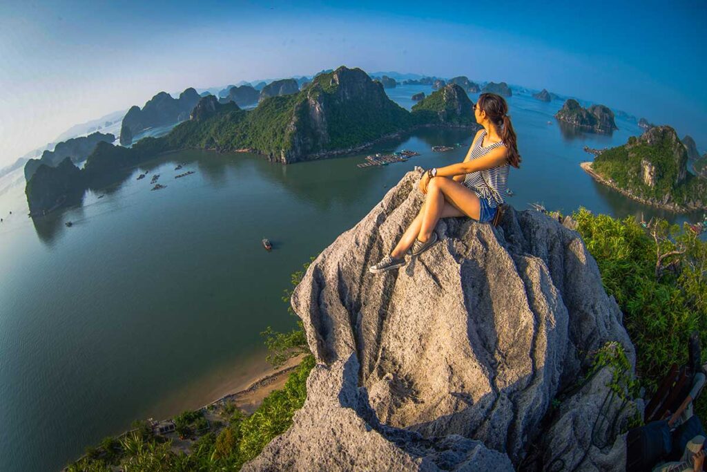 Solo female traveler sitting on a rock with a breathtaking panoramic view of Halong Bay in Vietnam.