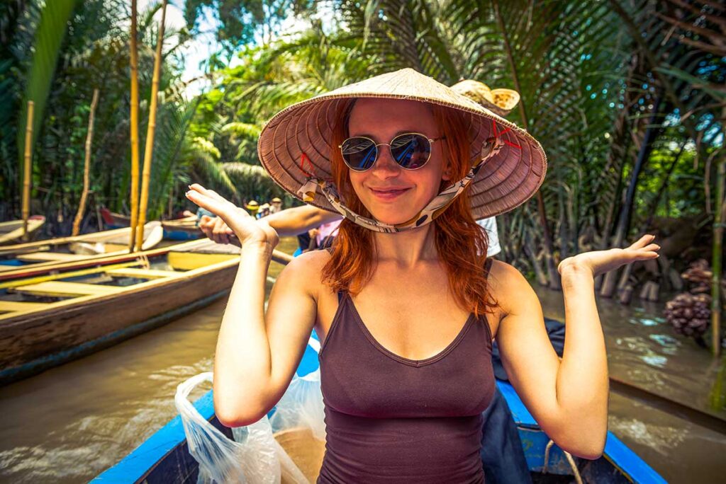 Female solo traveler in Vietnam wearing a conical hat, rowing through a picturesque canal in the lush Mekong Delta