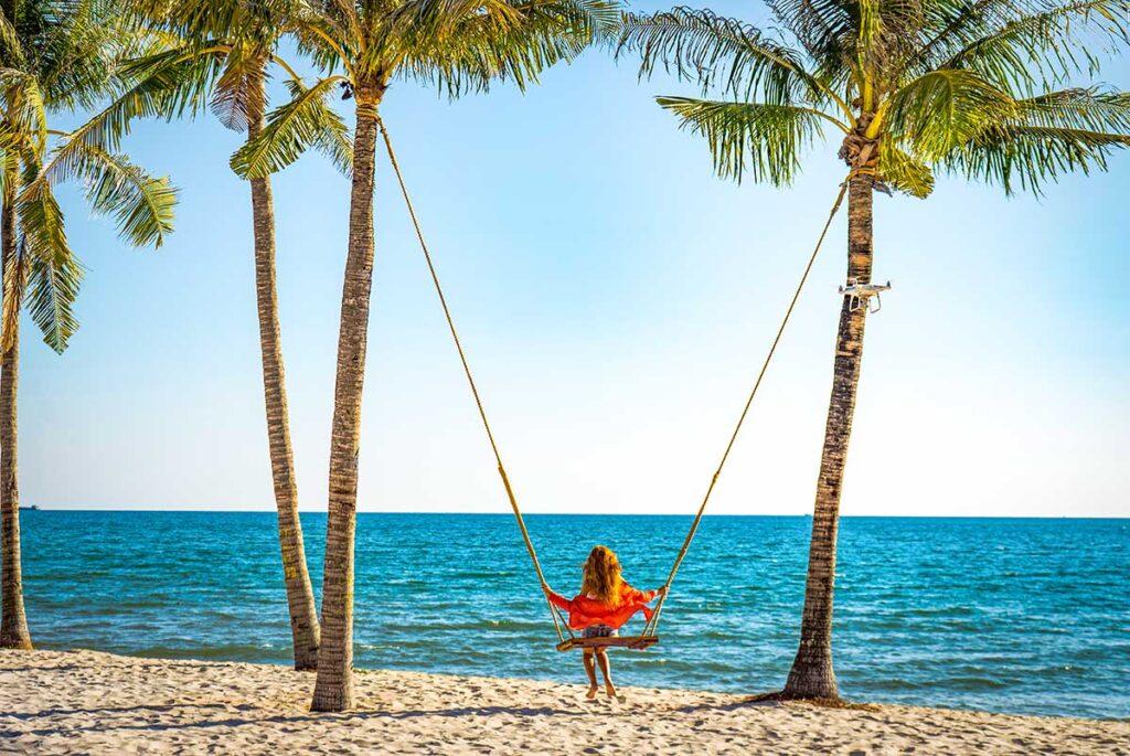 Solo female traveler in Vietnam sitting on a swing between two palm trees on the serene beach of Phu Quoc.