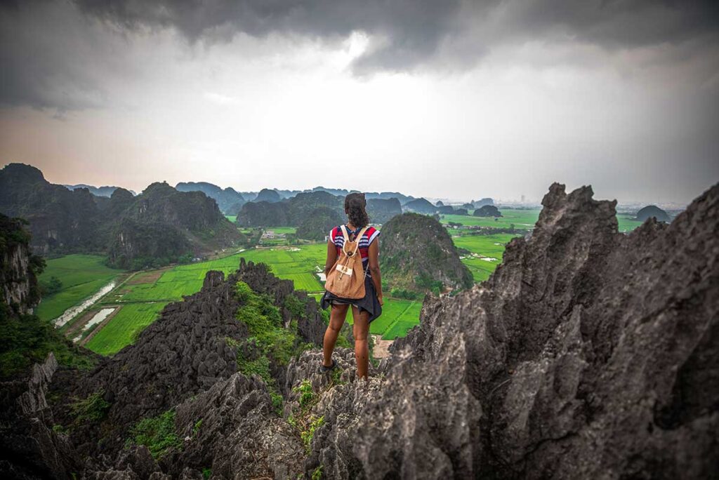 Solo female traveler standing on the rocks at Mua Cave viewpoint, overlooking the scenic landscape of Ninh Binh, Vietnam