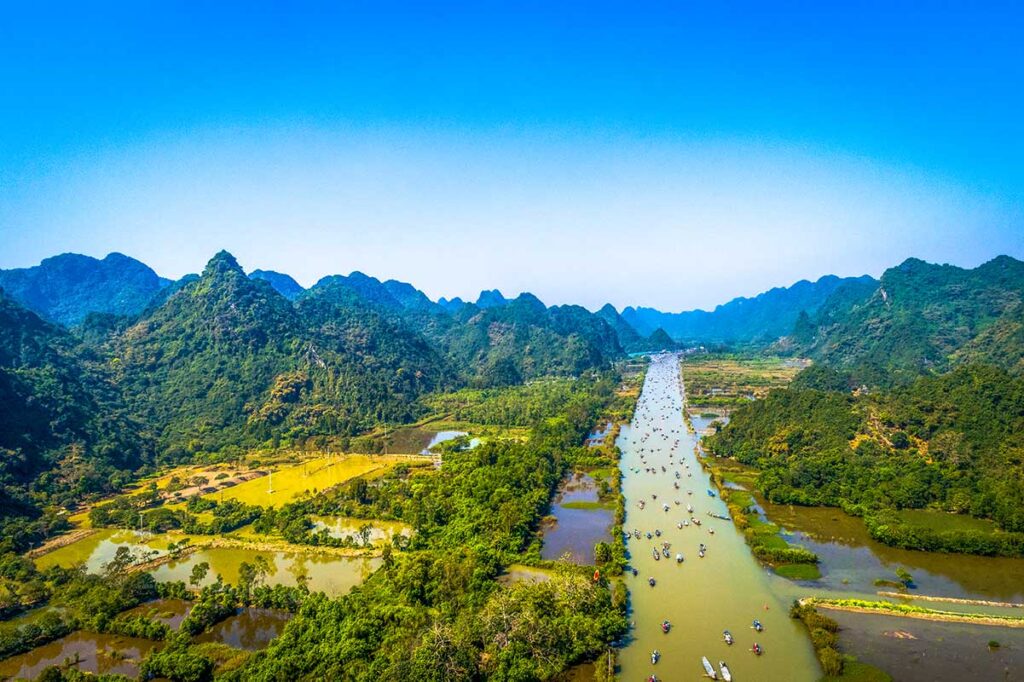 Yen Stream Boats to Perfume Pagoda: Boats filled with pilgrims and tourists navigate the Yen Stream, a tributary of the Red River, on their way to the Perfume Pagoda.