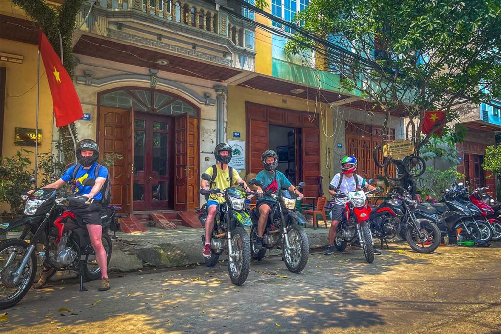 One foreigner sitting on a big motorbike and three other foreigners sitting on a dirt bike and at a motorbike rental in Cao Bang