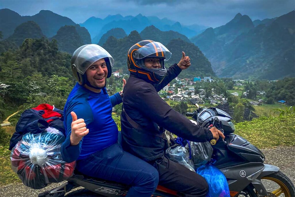 A tourist sitting on the back of a motorbike driven by a local experiences guide (also refered as Easy Rider)- A Cao Bang motorbike tour