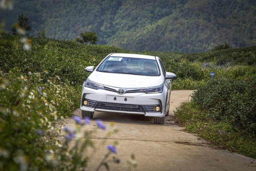 A car in Cao Bang that is rented including a driver for sightseeing in the province is driving over a small road with Cao Bang's mountains on the background