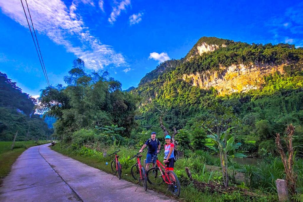 Two tourist stop cycling to see the breathtaking landscape of Ba Be National Park while holding their bikes