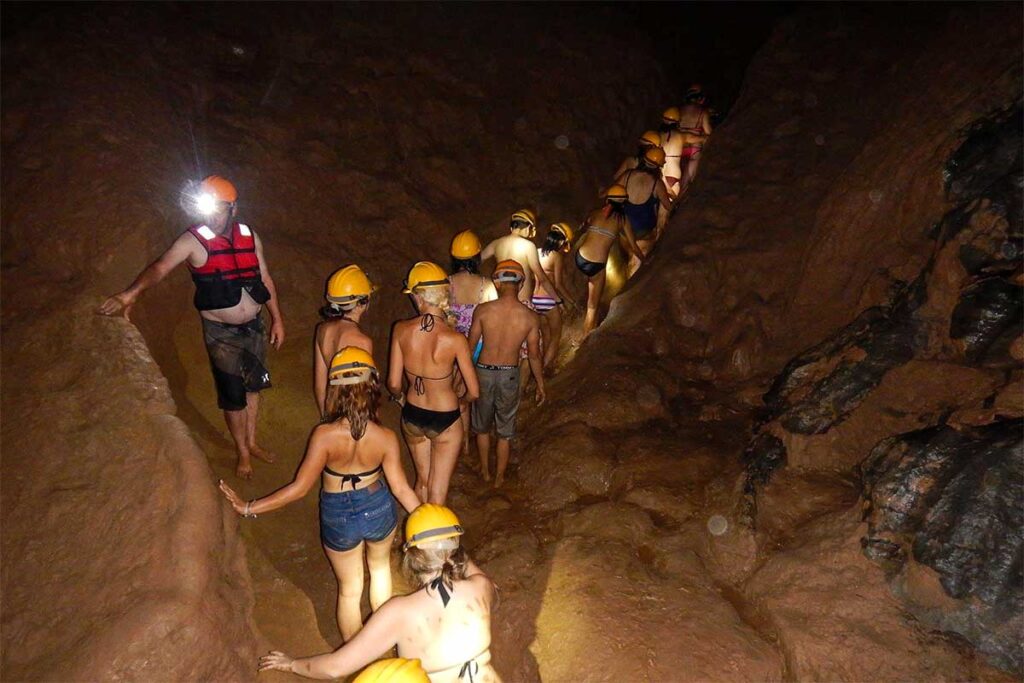 A group of travelers walking through a cave tunnel full of mud at the Dark Cave in Phong Nha National Park