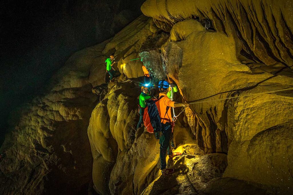 People using ropes to climb inside Hang Va Cave