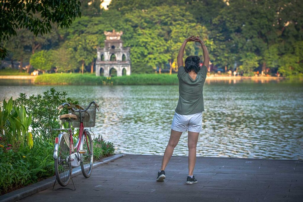 Hanoi n the morning at Hoan Kiem lake - A women stretching herself with bicycle next to her