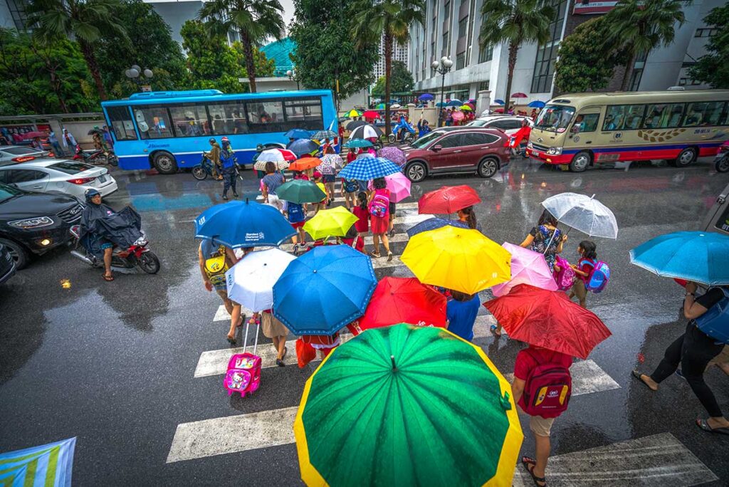 A lot of people are crossing the road with umbrellas during the rain in Hanoi