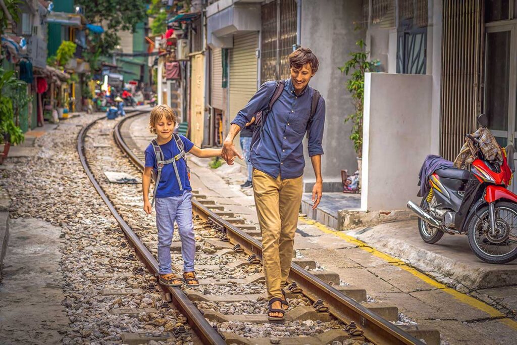 A farther and son walking over the train track in Hanoi Train Street, a fun sight to visit in Hanoi with kids