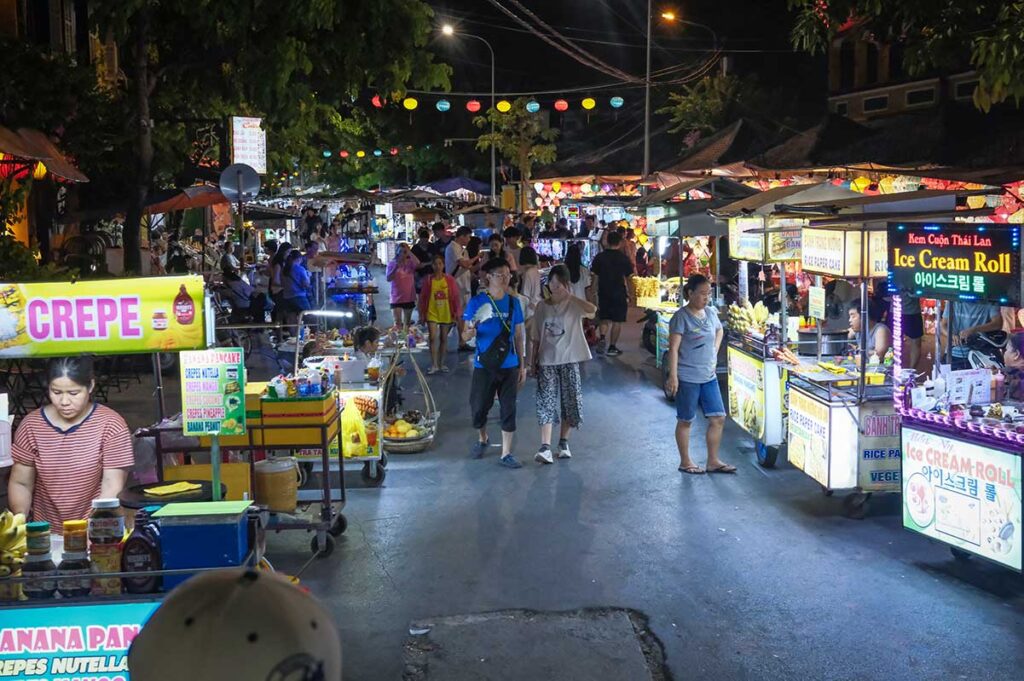 Crowded street of Hoi An Night Market with locals and tourists enjoying food stalls and colorful lanterns at night