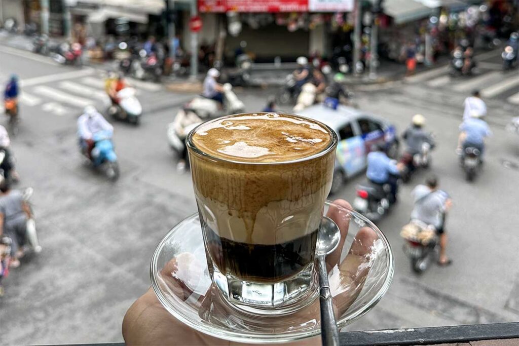 In Nang Cafe Hanoi a hand holding an egg coffee with on the background traffic of the Old Quarter 