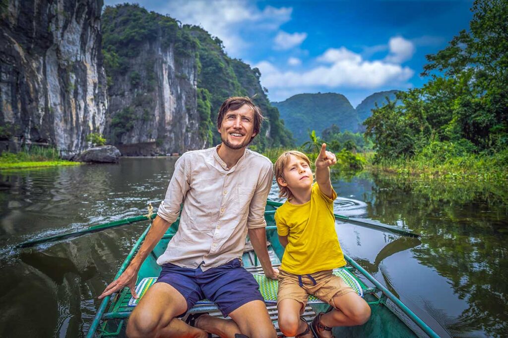 A farther and son sitting in a scenic boat ride in Trang An, one of the best things to do in Ninh Binh with kids