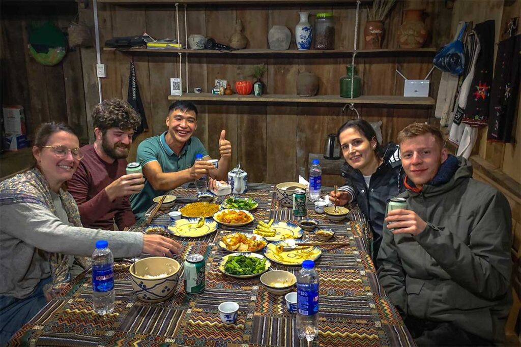 Foreign tourists sitting around a table eating and drinking with a local host at a homestay near Phia Oac National Park