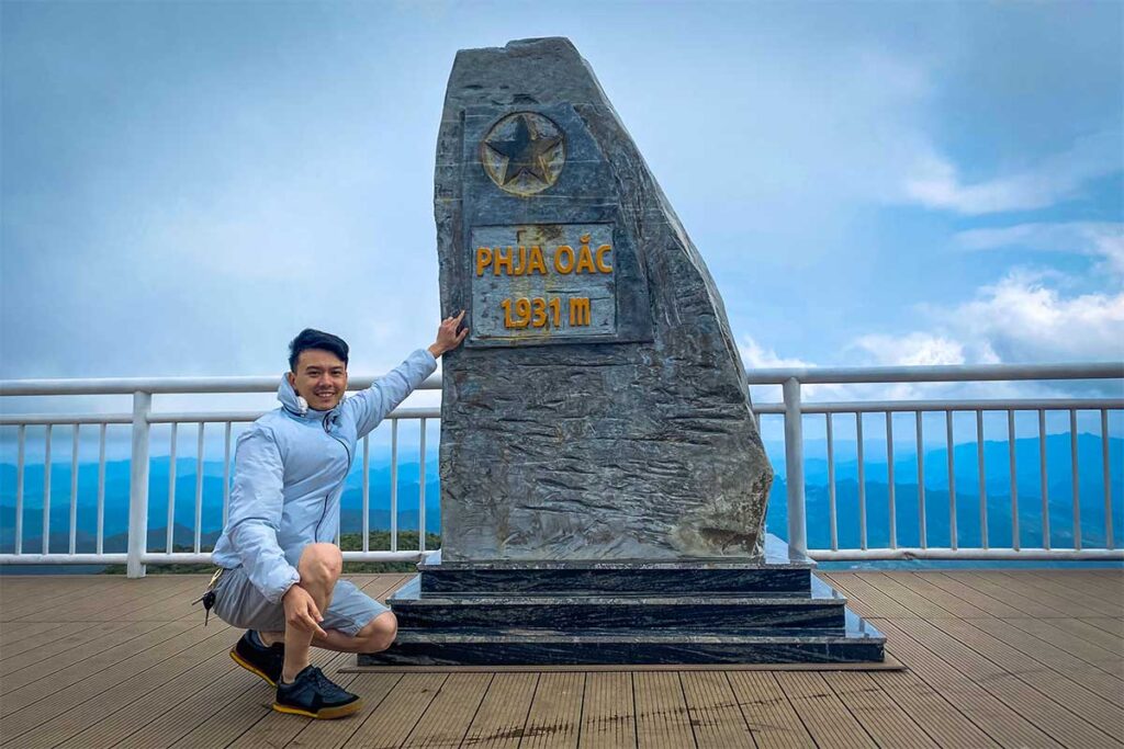 A man sitting at Phia Oac Peak - including a stone that indicated the height of the peak  with 1931 meter