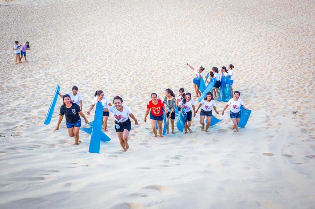 A group of Vietnamese sliding down the Quang Phu Sand Dunes in Quang Binh