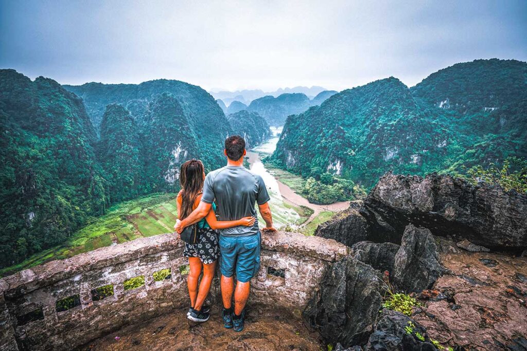 A romantic view of a couple on their honeymoon in Vietnam overlooking the rice fields from Mua Cave at sunset in Ninh Binh