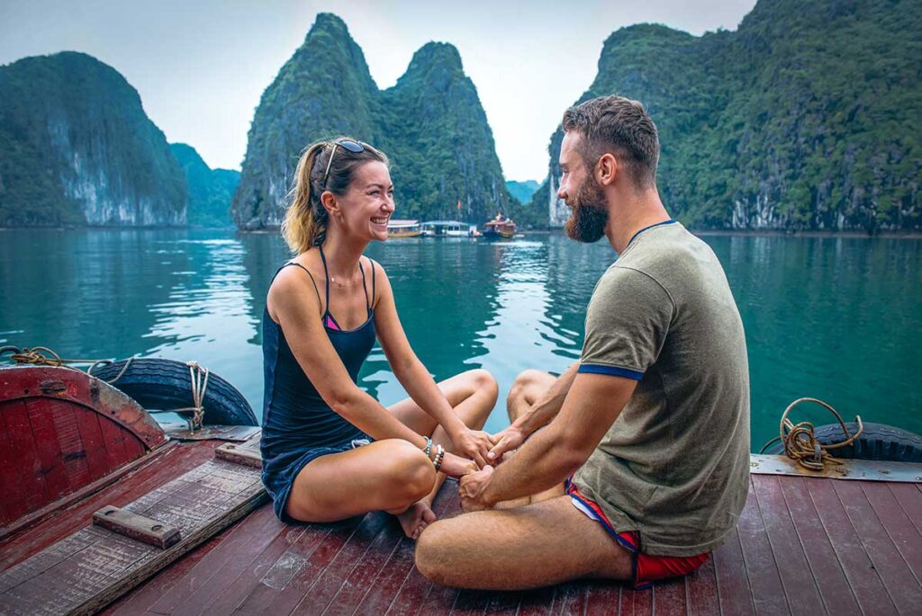 A couple sitting across each other holding hands on a boat in Halong Bay on their honeymoon in Vietnam