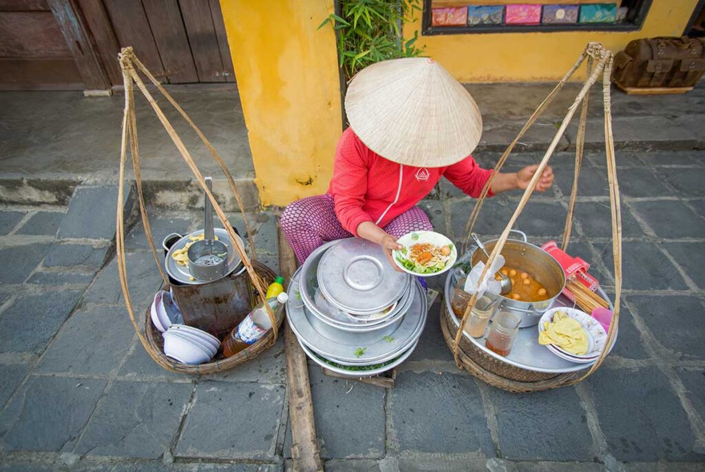 Local woman serving traditional street food in Hoi An – an essential thing to do for food lovers exploring Vietnam’s cuisine.