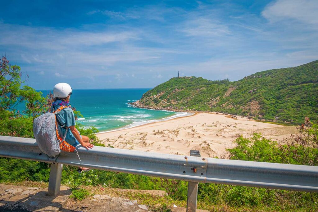 Traveler overlooking the Phu Yen coastal road with turquoise sea, sandy coves, and the iconic lighthouse, a popular day trip from Quy Nhon.