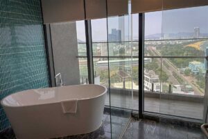 Modern Quy Nhon hotel bathroom with panoramic glass windows overlooking the city skyline and coastline, offering luxury sea-view stays.