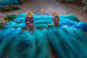 Two woman with conical hats are repairing fishnets in Bac Lieu province