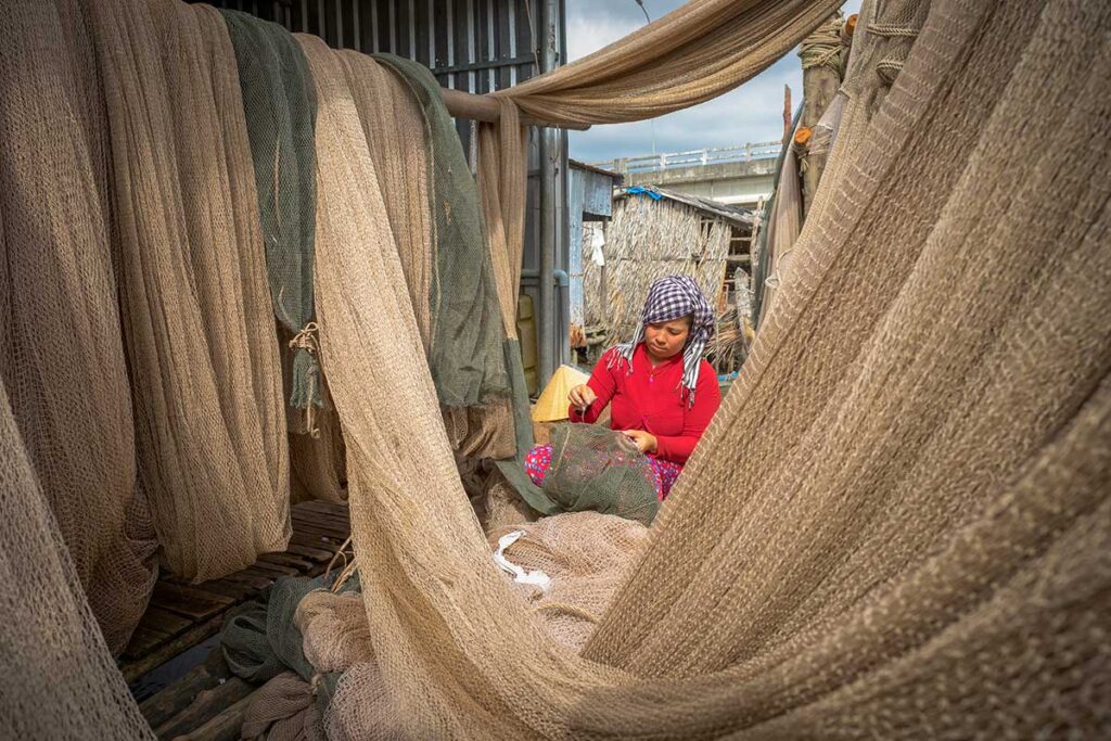 Local woman repairing fishing nets in Ca Mau, Vietnam, highlighting the province’s traditional fishing culture.