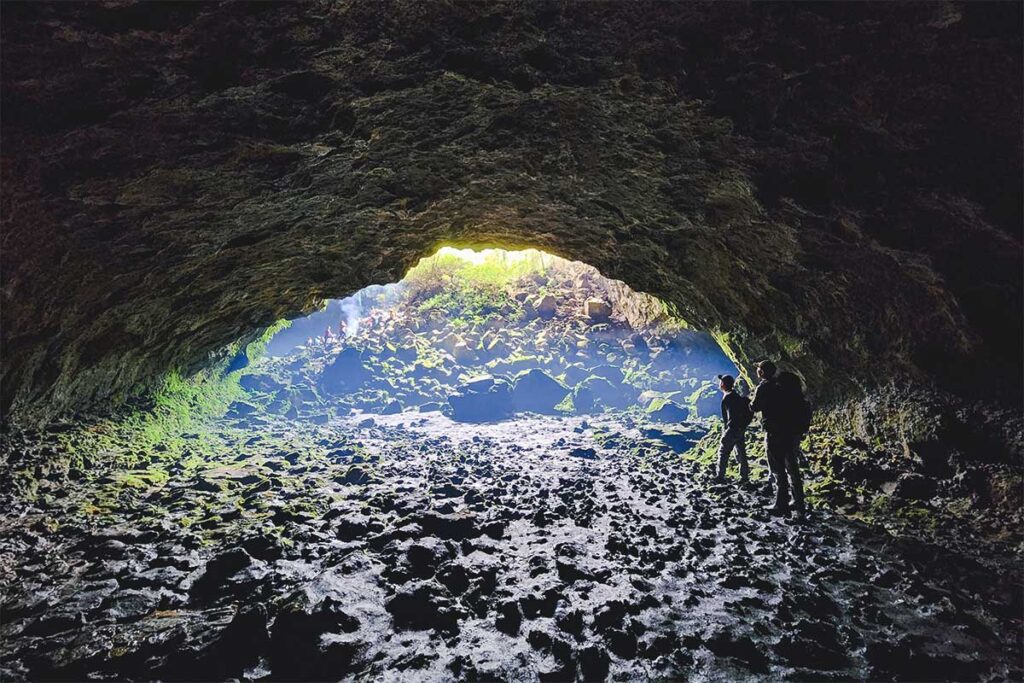 Two adventurous travelers navigating through a dark cave, believed to be part of the lava tunnel system in Chu Bluk Volcano area.