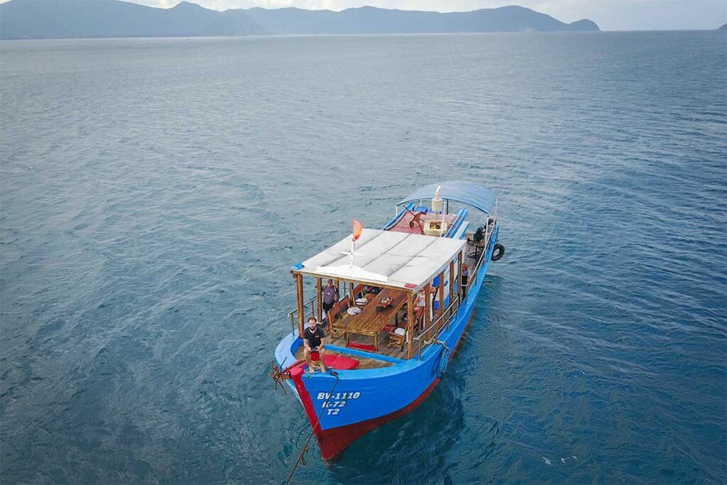 A drone view of a diving boat near Con Dao, floating over the turquoise waters, surrounded by the island’s stunning marine environment.