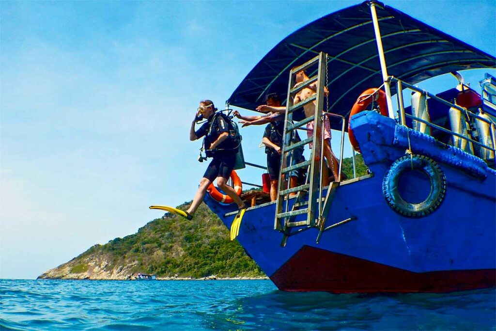 A scuba diver jumps from a boat into the clear waters of Con Dao, fully equipped with diving gear, ready to explore the vibrant marine life.