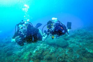 Con Dao in June – Two divers hold hands underwater, exploring the vibrant marine life during one of the best diving months in Con Dao.