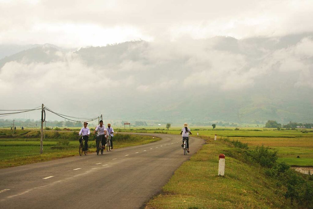 A peaceful rural road meandering through the countryside of Dak Lak, surrounded by lush fields and traditional villages.