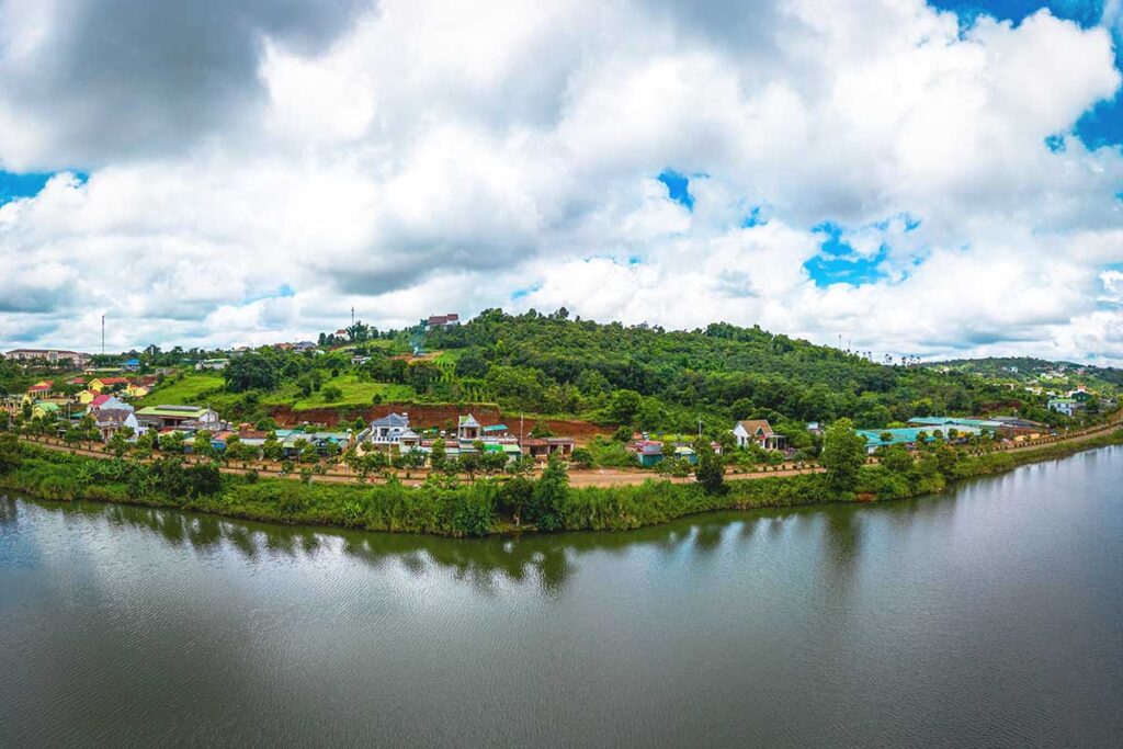 A peaceful view of Dak Mil Lake with a small village nestled along its shore, reflecting rural life in Dak Nong Province.