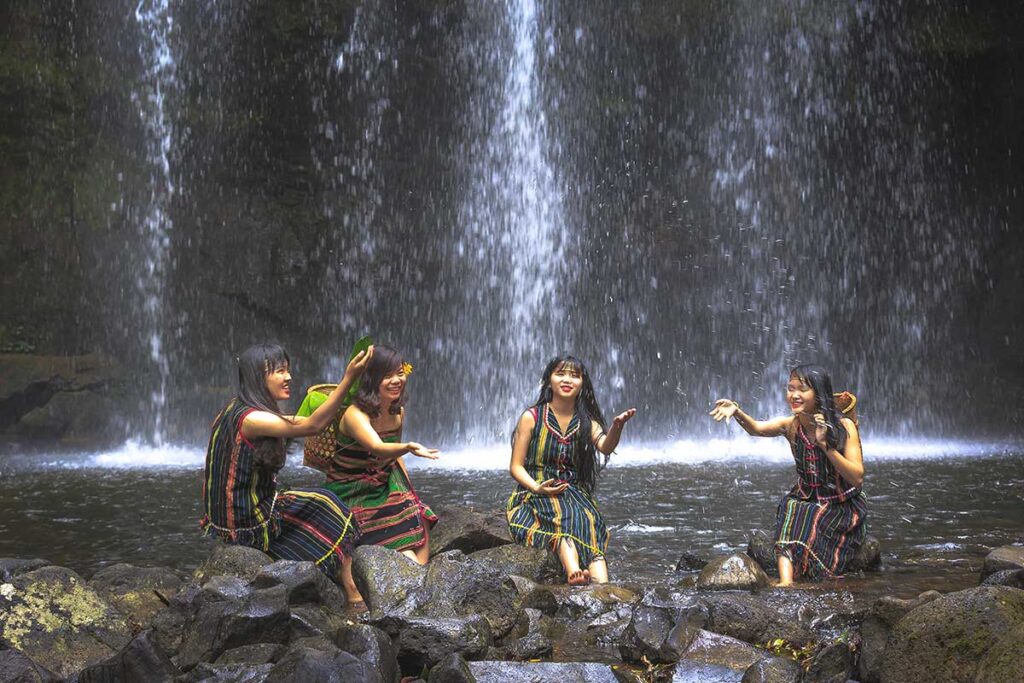 A woman from an ethnic minority group sitting in a natural pool at the base of a waterfall, surrounded by untouched nature.