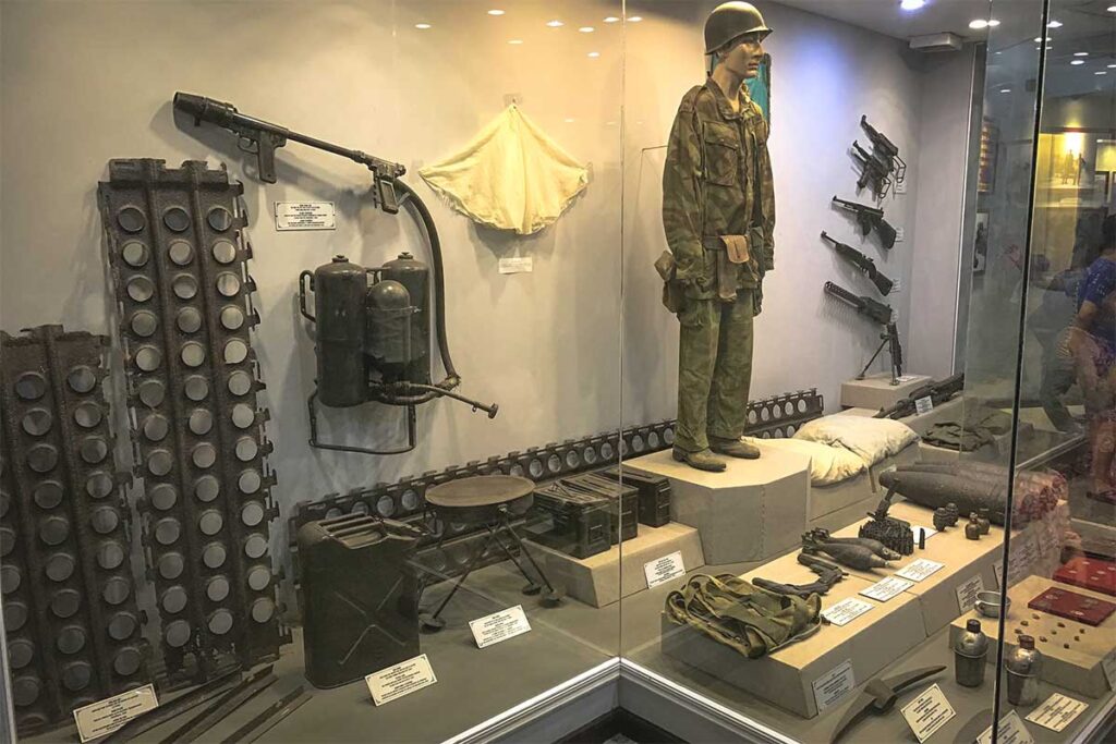 A display inside the Dien Bien Phu Victory Museum, showcasing a soldier's equipment, including various weapons and a flamethrower.