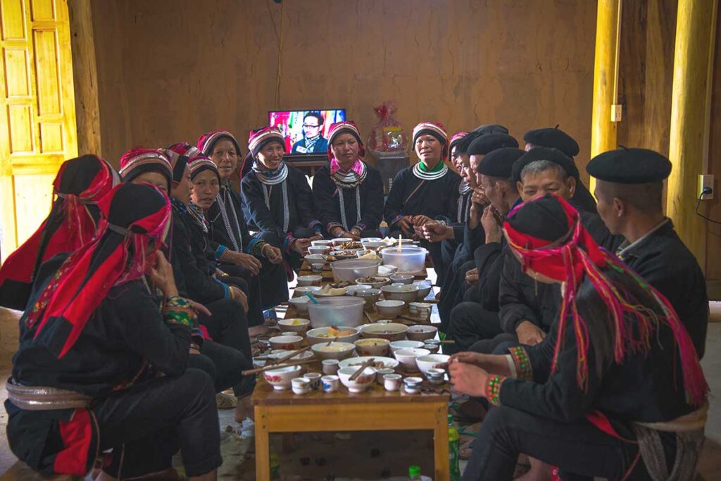 A large group of Dao ethnic women gathered in a traditional home, enjoying a Tet holiday feast together in Ha Giang.