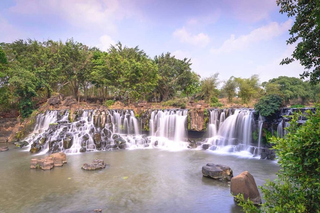 A scenic view of Giang Dien Waterfall, with cascading water flowing over rocky formations, surrounded by lush vegetation.