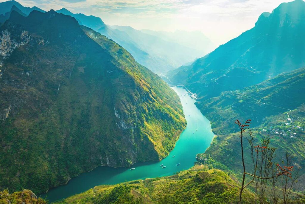 Ha Giang Loop in August – A spectacular view of the Nho Que River from Ma Pi Leng Pass, with lush green mountains and sunlight breaking through the clouds, highlighting the natural beauty of Ha Giang Loop in August.