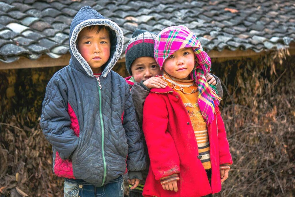 Three ethnic minority children wearing thick warm jackets, braving the cold winter temperatures in Ha Giang.