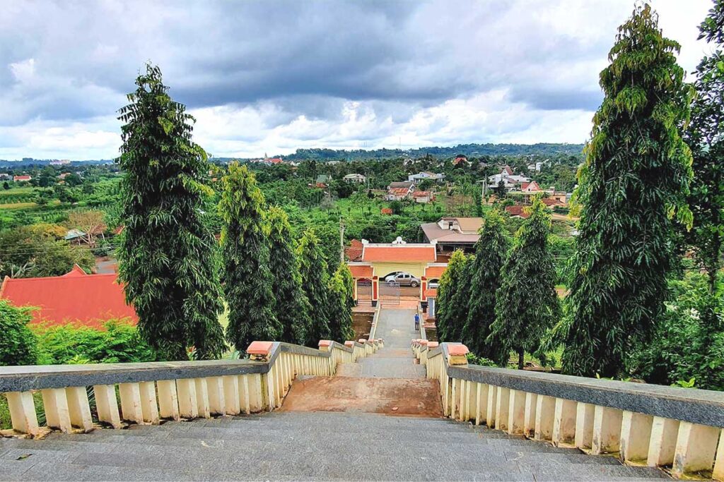 A scenic overlook from Hill 722 in Dak Sak, showing the stairway leading up, the entrance gate below, and a small village in the distance.