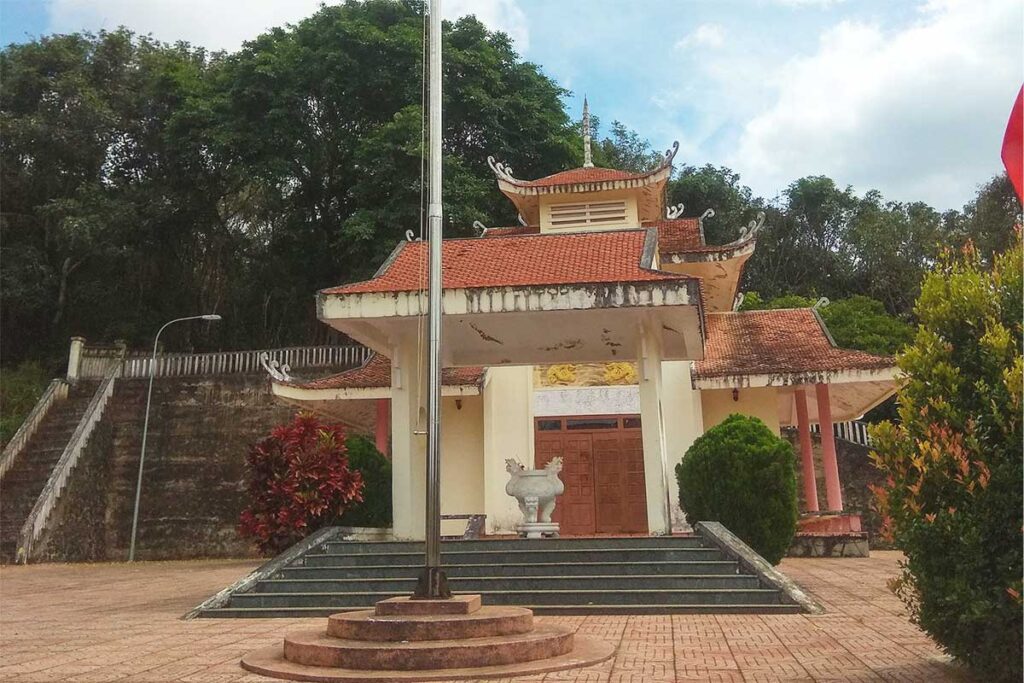 A flag flying high beside a temple-like shrine on top of Hill 722, a significant historical site in Dak Sak.