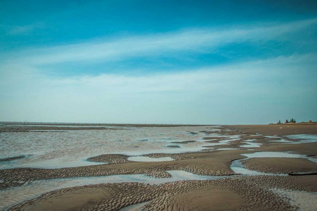 Low-tide view of Ho Be Beach in Soc Trang with sand ripples, shallow tidal pools, and a wide-open