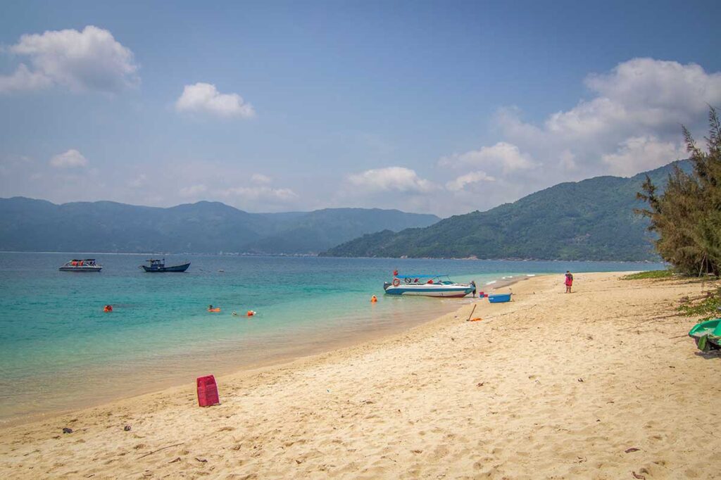 Hon Nua Island near Phu Yen with white sandy beach, clear blue water, and tour boats anchored along the shore.