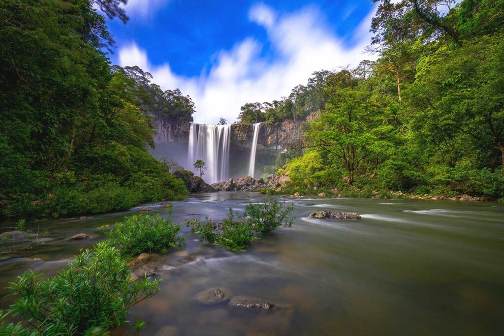 A slightly distant view of K50 Waterfall, framed by thick rainforest, highlighting its remote and untouched beauty.