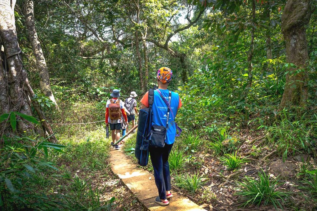 Hikers walking along a narrow jungle trail, exploring the lush wilderness of Kon Chu Rang Nature Reserve.