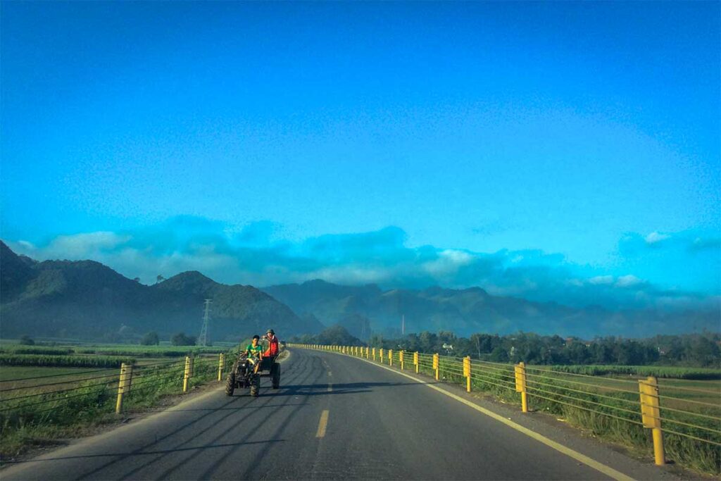 Road leading to rural Lac Son District with a small basic tractor with locals driving