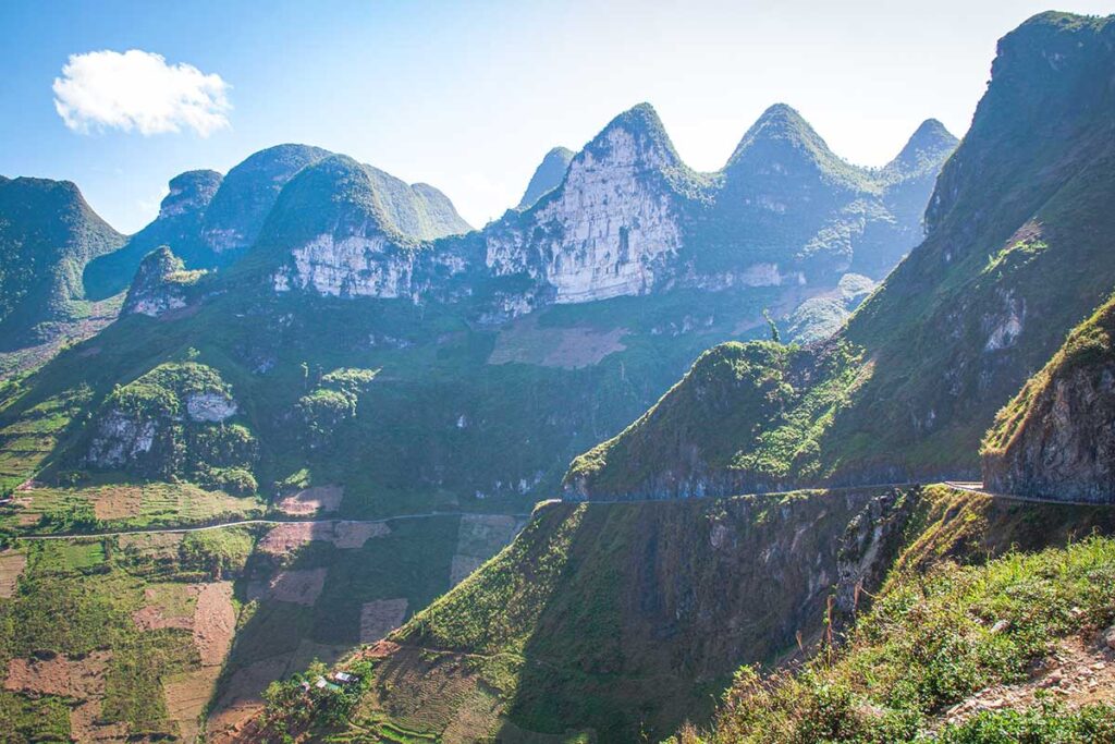 A stunning clear day showcasing the layered mountain contours of Ma Pi Leng Pass, with a winding road carved into the cliffs.