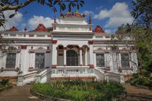 Colonial-era Huynh Ky Mansion in Tra Vinh with European-inspired architecture, red and white detailing, and a garden entrance.