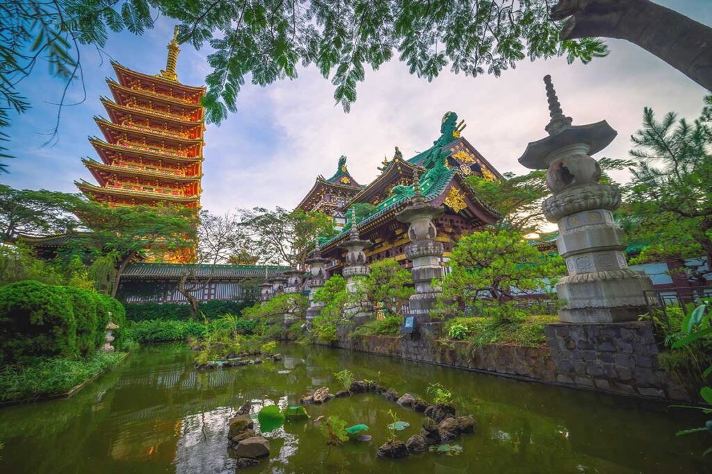 A tranquil pond with a temple and towering stupa in the background, located inside Minh Thanh Pagoda.