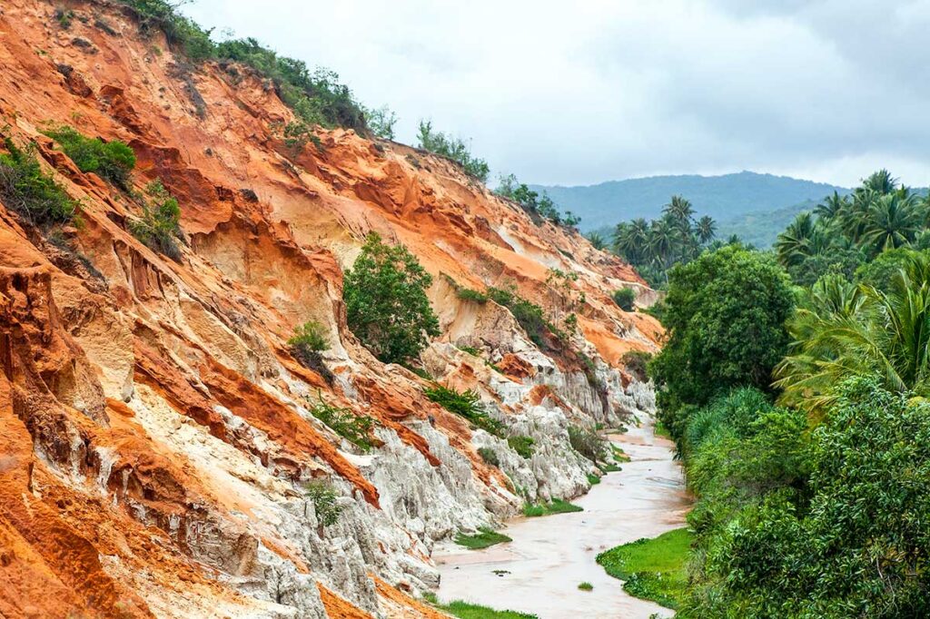 Mui Ne in June: A cloudy day at the Fairy Stream in Mui Ne in June, with soft light casting a muted tone over the red and white sand formations, creating a peaceful atmosphere.